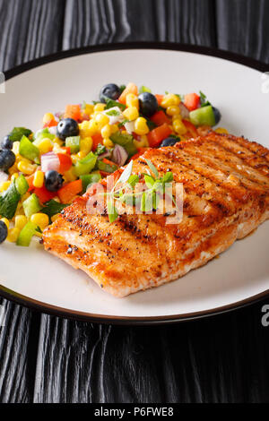 Gegrillter Lachs mit Salat Salsa an Gemüse und Beeren in der Nähe serviert auf einem Teller auf den Tisch. Vertikale Stockfoto