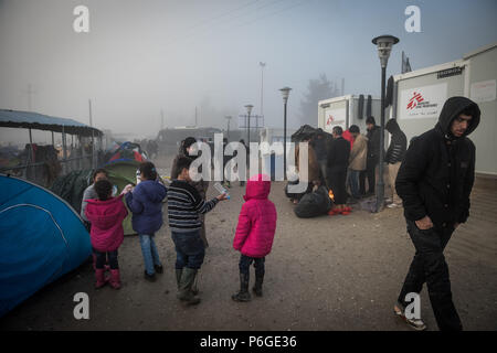 Flüchtling versuchen sich zu warm und trocken Sie feuchte Tücher vom Lagerfeuer nach einem Regen Nacht im provisorischen Flüchtlingslager der Greek-Macedonian bord Stockfoto