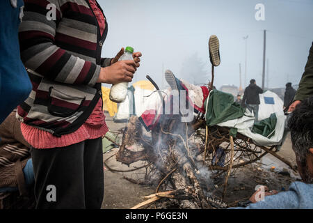 Flüchtling versuchen sich zu warm und trocken Sie feuchte Tücher vom Lagerfeuer nach einem Regen Nacht im provisorischen Flüchtlingslager der Greek-Macedonian bord Stockfoto