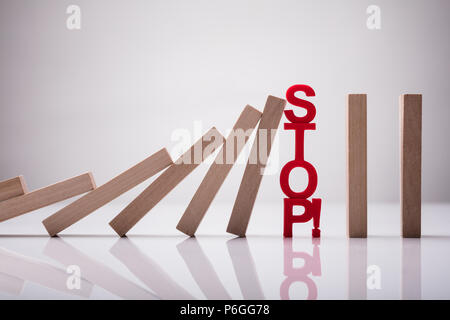 In der Nähe von Dominos fallen Gestoppt durch Stop Text auf reflektierenden Boden Stockfoto