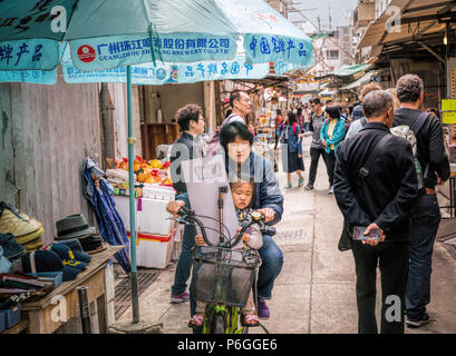 19. Februar 2018 - Lantau Island, Hong Kong. Asiatische Frau Radfahren in der Dorfstraße von Tai O mit Kind auf dem Fahrrad. Stockfoto
