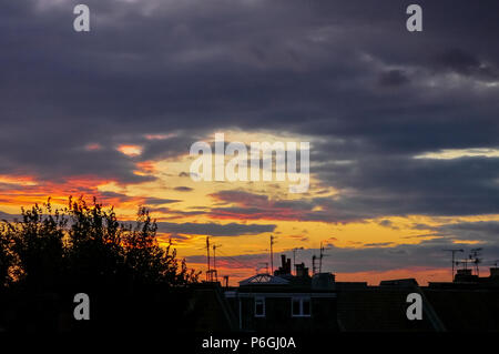 Silhouetted Bäume und Fernsehantennen auf den Dächern in einer englischen Stadt bei Sonnenuntergang Stockfoto