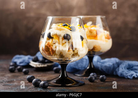 Gesunde hausgemachte layered Dessert trifle mit Orange, Heidelbeere, Keksen, Joghurt und Müsli in einem Gläser Stockfoto