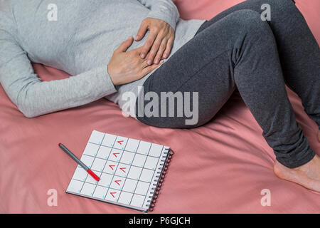 Schmerzen im Unterleib, die während des Zeitraums der Frau. Monatliche beunruhigt. Kalender mit markierten Tage der Menstruation. Stockfoto