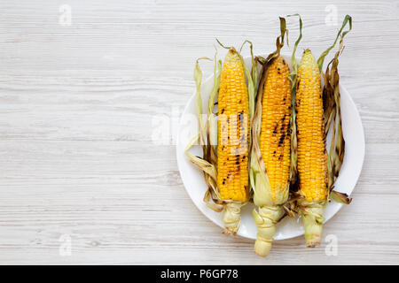 Gegrillte Maiskolben auf einer runden Platte über weiße Holz- Oberfläche, Ansicht von oben. Von oben, Overhead, flach. Kopieren Sie Raum und Text. Stockfoto