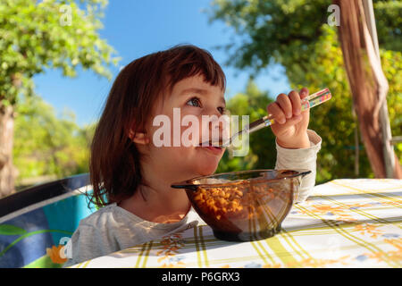 Süße kleine Mädchen essen Cornflakes mit Milch. Sommer sonnigen Tag im Garten. Stockfoto