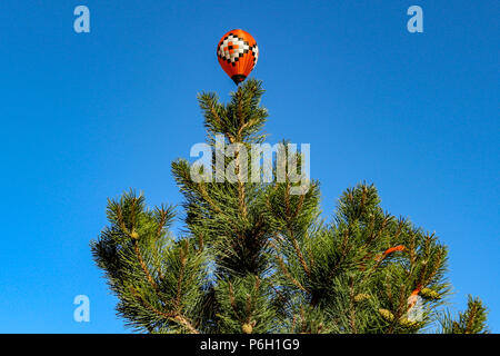 Rote Heißluftballon über Cedar Tree sieht aus wie ein Christmas Ornament. Foto bei der New Mexico Albuquerque International Balloon Festival übernommen. Stockfoto