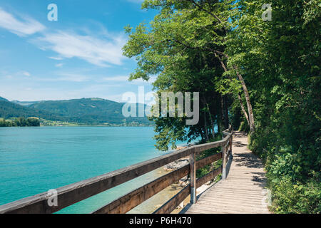 Steg am Rand der türkisfarbenen See namens Wolfgangsee Berge im Hintergrund und Wolken am Himmel Stockfoto