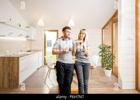 Portrait einer jungen und glückliches Paar stehen zusammen mit Kaffee im Speisesaal des modernen Holz- Country House Stockfoto