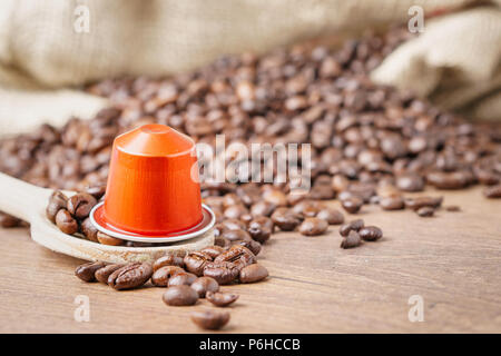 Im Vordergrund ein Kaffee Kapsel auf Holzlöffel und geröstete Kaffeebohnen mit sackleinen Sack auf blur Holz- Hintergrund, aus der Nähe. Stockfoto