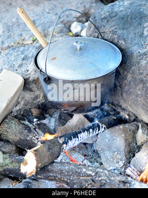 Kochen im Kessel über dem offenen Feuer. Vorbereiten der Nahrung an der Stange in ein wildes Campen. Abendessen in einem Topf auf Feuer zu kochen. Draußen in den Campingplatz zu essen. Stockfoto