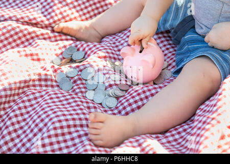 Baby Junge sitzt auf der Picknickdecke setzenden Münzen im Sparschwein Stockfoto