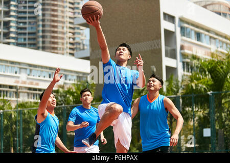 Jungen asiatischen erwachsenen männlichen Spieler spielt Basketball auf einem städtischen Außenplatz. Stockfoto