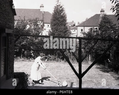 1950er Jahre, Dame außerhalb an einem sonnigen Tag den Rasen mäht mit einer Hand Rasenmäher. Stockfoto