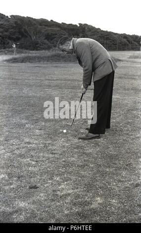 1950er Jahre, einem erwachsenen Mann wearig Jacke und Hose draußen stehen auf Gras, das ein Golf Ball. Stockfoto