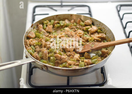 Holzspatel rühren frango com quiabo (portugiesisch für "Huhn mit Okra'), brasilianisches Gericht kochen in saute Pan Am Herd Stockfoto