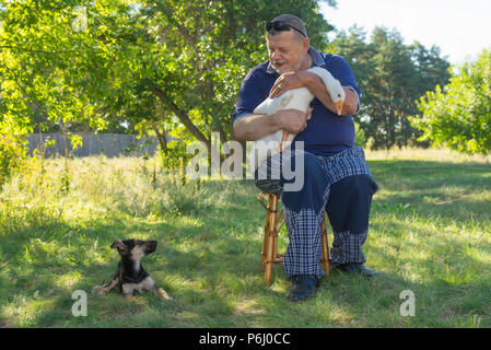 Schöne Outdoor Portrait von älterer Mann seine niedlichen Welpen neben ihm saß und weiße Gans auf den Händen Stockfoto