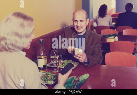 Positive senior Paar beschäftigt mit Handys auf Datum im Cafe Stockfoto