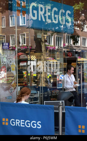 Die Leute sitzen außerhalb des Take-away Food Shop, Sandwichmaker und Bäckerei Greggs, der Tottenham Court Road im Zentrum von London. Stockfoto