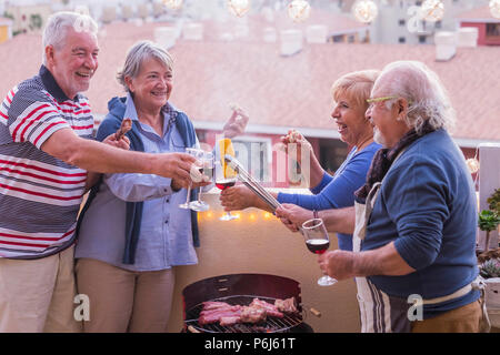 Vier aktive ältere zog sich viel Spaß auf der Terrasse zu Hause kochen einige bbq jeder lächelt und in Freundschaft bleiben unter einen schönen sonnigen Tag. Stockfoto