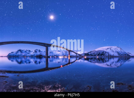 Brücke und lila Sternenhimmel mit schönen Spiegelbild im Wasser. Nacht Landschaft mit Brücke, schneebedeckte Berge, Himmel mit Mond und helle Sterne Ref. Stockfoto