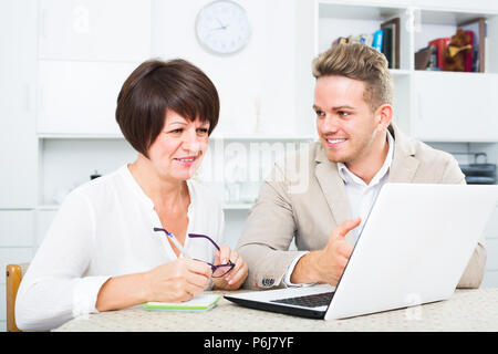 Fröhliche Mutter und Sohn betrachten, neue Software auf dem Laptop am Tisch sitzen Stockfoto