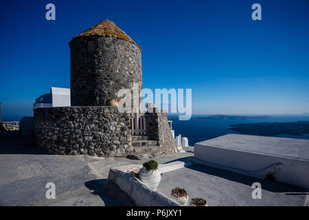 Typische Gebäude aus Stein mit Reetdach - getreidespeicher - Hotel in Santorini, Griechenland, mit Blick aufs Meer und Felsen im Hintergrund. Stockfoto