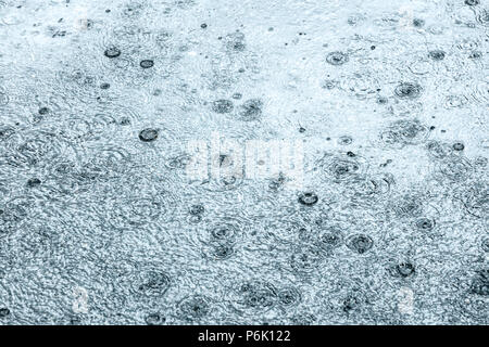 Die Regentropfen fallen auf überfluteten Asphalt erzeugen Blasen Stockfoto