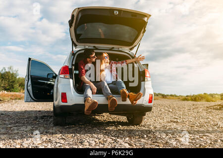 Happy Traveler Paar im Auto open Trunk sitzen und den Sonnenaufgang beobachten Stockfoto