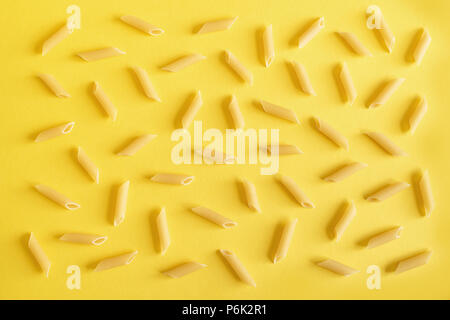 Penne Pasta auf gelbem Hintergrund, Ansicht von oben, flach. Stockfoto