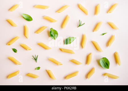 Penne Pasta auf Rosa pastell Hintergrund, Ansicht von oben, flach. Muster Ungekochte Nudeln mit Kräutern, Basilikum und Rosmarin. Stockfoto