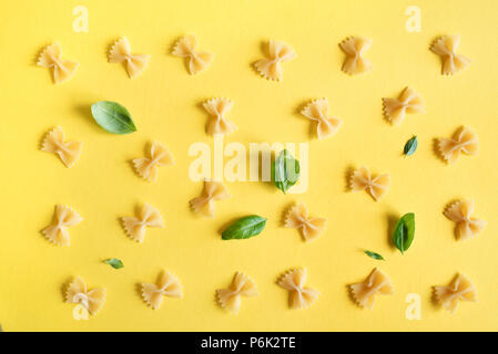 Farfalle Pasta auf gelbem Hintergrund, Ansicht von oben, flach. Muster Ungekocht farfalle Nudeln mit Basilikum. Stockfoto