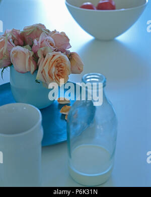 Still-Life aus Rosen in Weiß Schale auf dem Tisch mit einer Flasche Milch und weiße Tasse Stockfoto