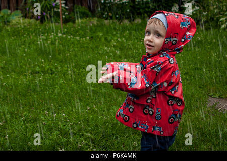 Little Boy in eine wasserdichte Jacke bei Traktoren, die mit dem Regen. Kind Spaß im Freien im Sommer. Stockfoto