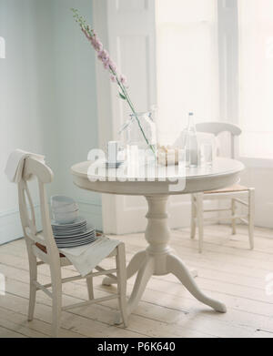 Stapel Schüsseln und Teller auf Weiß lackiert Stuhl am kreisförmigen weißer Tisch im Esszimmer mit weiß lackierten Holzboden Stockfoto
