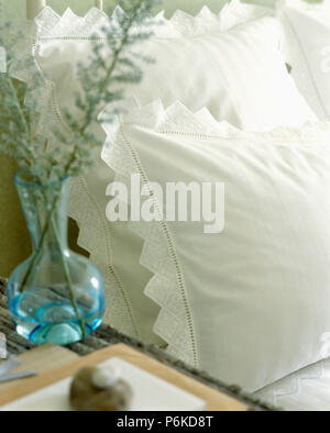 In der Nähe von Laub in blauem Glas Vase auf dem Tisch neben dem Bett mit weißer Broderie anglaise getrimmt Kissen Stockfoto