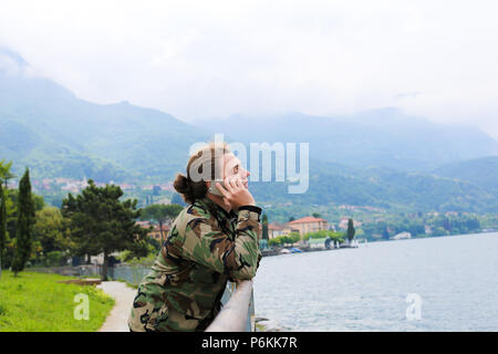 Jungen kaukasischen Mann durch Smartphone in der Nähe von Bannister, den Comer See und Alpen Berg im Hintergrund. Stockfoto