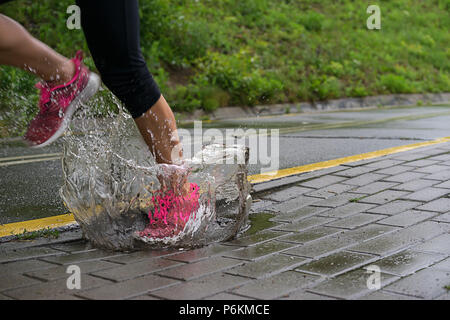 Einzelläufer laufen im Regen und macht Sprung in Pfütze Stockfoto