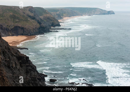 Sandstrand mit felsigen Bergrücken trübes Wetter Aussicht auf Sommer Atlantic an der felsigen Küste (Costa Vicentina, Algarve, Portugal). Und Ocean Surf Wellen. Stockfoto