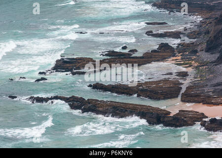 Sandstrand mit felsigen Bergrücken trübes Wetter Aussicht auf Sommer Atlantic an der felsigen Küste (Costa Vicentina, Algarve, Portugal). Und Ocean Surf Wellen. Stockfoto
