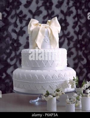 In der Nähe von Three-tier iced Hochzeitstorte auf Tabelle mit Schneeglöckchen in kleinen weißen Vasen Stockfoto