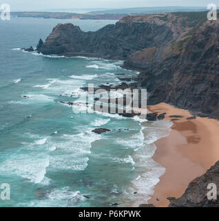 Sandstrand mit felsigen Bergrücken trübes Wetter Aussicht auf Sommer Atlantic an der felsigen Küste (Costa Vicentina, Algarve, Portugal). Und Ocean Surf Wellen. Stockfoto