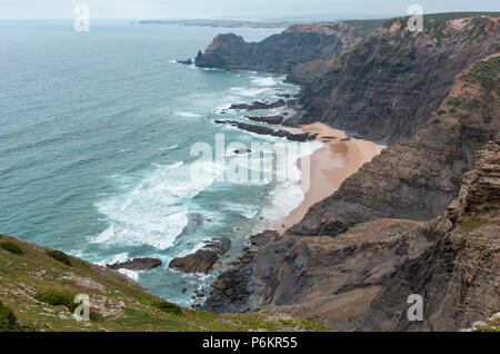 Sandstrand mit felsigen Bergrücken trübes Wetter Aussicht auf Sommer Atlantic an der felsigen Küste (Costa Vicentina, Algarve, Portugal). Und Ocean Surf Wellen. Stockfoto