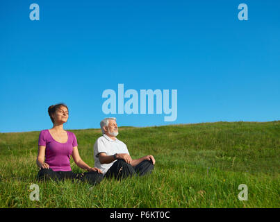 Junge Mädchen und alte Menschen meditieren sitzt in das Feld ein. Im Lotussitz auf helle, gesättigte Himmel Hintergrund. Positiv, zufrieden, das gute Gefühl, konzentriert. Ruhe und Stille. Stockfoto