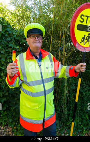 Iollipop Mann, der gerade seine Schicht an der Schule überqueren Zebrastreifen abgeschlossen hat. Er ist Abkühlung mit einem Lutscher das in derselben Farbe wie sein Outfit. England, Großbritannien Stockfoto