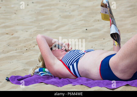 Bournemouth, Dorset, Großbritannien. 1. Juli 2018. UK Wetter: diesig Sonnenschein, aber immer noch warm wie Tausende von sunseekers Kopf bis zu den Stränden von Bournemouth ein Tag am Meer genießen. Frau Sonnenbaden lesen Magazin. Credit: Carolyn Jenkins/Alamy leben Nachrichten Stockfoto