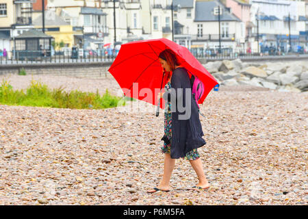 Honiton, Devon, Großbritannien. 1. Juli 2018. UK Wetter. Eine Frau auf dem Strand im Badeort Sidmouth Devon mit Schirm, der als die Stadt fängt den Rand eines vorbeifahrenden heftiger Regenschauer. Foto: Graham Jagd-/Alamy leben Nachrichten Stockfoto