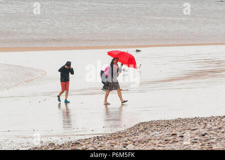 Honiton, Devon, Großbritannien. 1. Juli 2018. UK Wetter. Eine Frau auf dem Strand im Badeort Sidmouth Devon mit Schirm, der als die Stadt fängt den Rand eines vorbeifahrenden heftiger Regenschauer. Foto: Graham Jagd-/Alamy leben Nachrichten Stockfoto