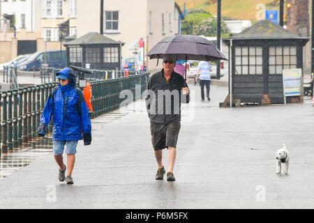 Honiton, Devon, Großbritannien. 1. Juli 2018. UK Wetter. Hund Spaziergänger am Meer am Badeort Sidmouth Devon mit einem Regenschirm, der als die Stadt fängt den Rand eines vorbeifahrenden heftiger Regenschauer. Foto: Graham Jagd-/Alamy leben Nachrichten Stockfoto