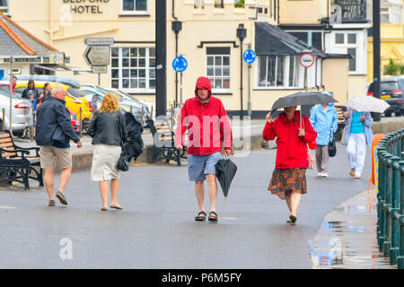 Honiton, Devon, Großbritannien. 1. Juli 2018. UK Wetter. Besucher in den Badeort Sidmouth Devon mit Sonnenschirmen, wie die Stadt fängt den Rand eines vorbeifahrenden heftiger Regenschauer. Foto: Graham Jagd-/Alamy leben Nachrichten Stockfoto